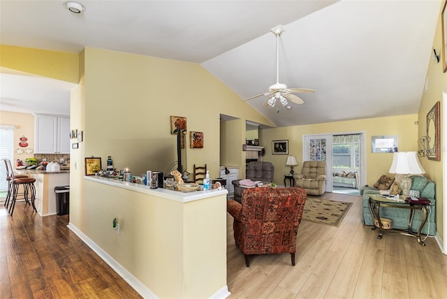 living area with baseboards, wood finished floors, ceiling fan, and vaulted ceiling