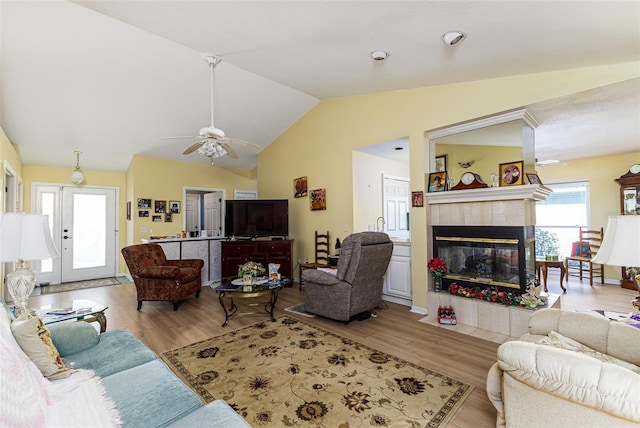 living area with vaulted ceiling, a tile fireplace, ceiling fan, and wood finished floors