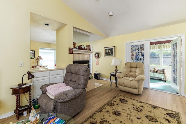 interior space with baseboards, lofted ceiling, wood finished floors, and a tiled fireplace