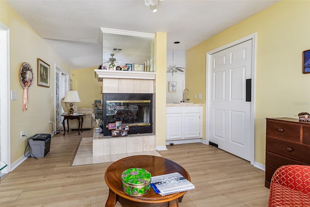 living area with ceiling fan, baseboards, light wood finished floors, and a tile fireplace