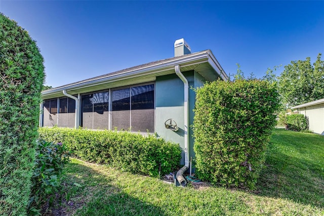 view of side of property featuring stucco siding, a lawn, a chimney, and a sunroom