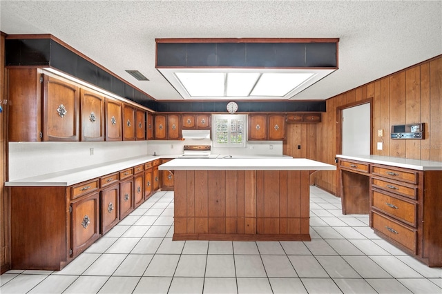 kitchen featuring stove, light tile patterned flooring, wooden walls, and a center island