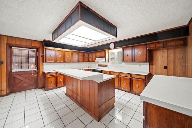 kitchen with electric range oven, a textured ceiling, a kitchen island, wooden walls, and light tile patterned floors