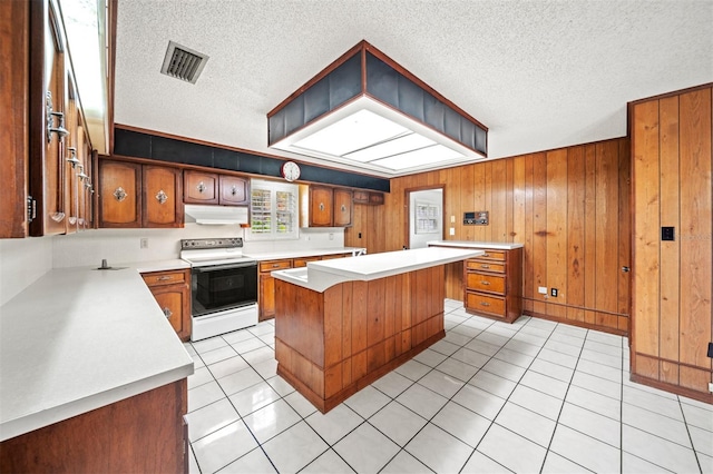 kitchen with a textured ceiling, a center island, wooden walls, electric range, and light tile patterned floors