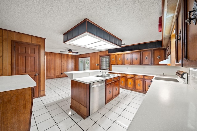 kitchen featuring ceiling fan, dishwasher, wood walls, a center island with sink, and sink