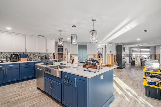 kitchen with pendant lighting, an island with sink, sink, stainless steel dishwasher, and blue cabinets