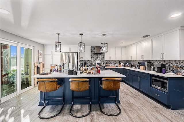 kitchen featuring white cabinets, decorative light fixtures, stainless steel appliances, blue cabinetry, and a center island with sink