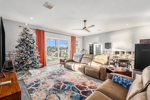 living room with a textured ceiling, ceiling fan, and light hardwood / wood-style floors