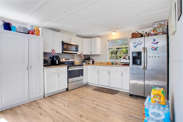 kitchen featuring light stone counters, stainless steel appliances, white cabinets, and light hardwood / wood-style flooring