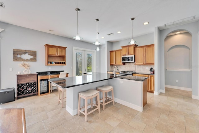 kitchen with sink, a kitchen island with sink, hanging light fixtures, stainless steel appliances, and french doors