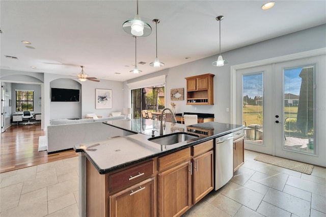 kitchen with dishwasher, sink, dark stone counters, a kitchen island with sink, and french doors