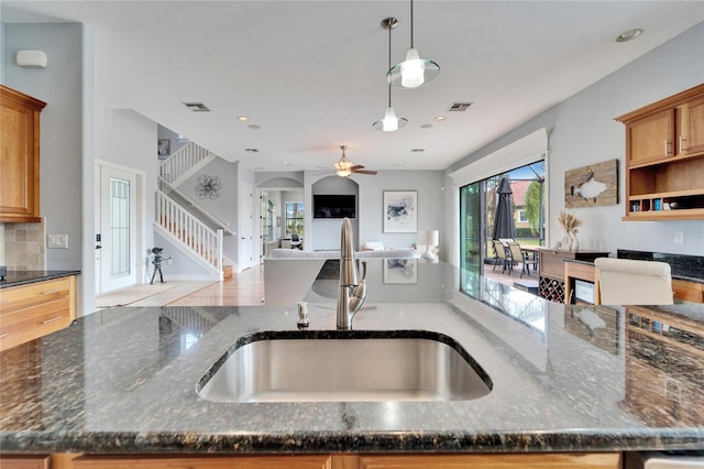 kitchen featuring sink, backsplash, dark stone counters, and decorative light fixtures