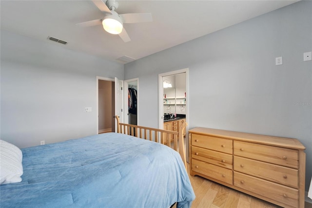 bedroom with ceiling fan, a walk in closet, ensuite bath, and light hardwood / wood-style flooring