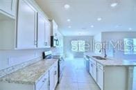 kitchen with light stone countertops, light tile patterned floors, sink, white cabinetry, and stove