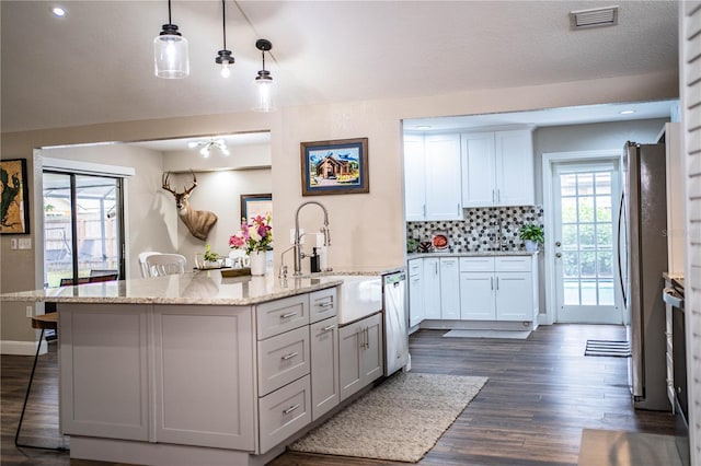 kitchen with tasteful backsplash, pendant lighting, white cabinetry, light stone countertops, and appliances with stainless steel finishes