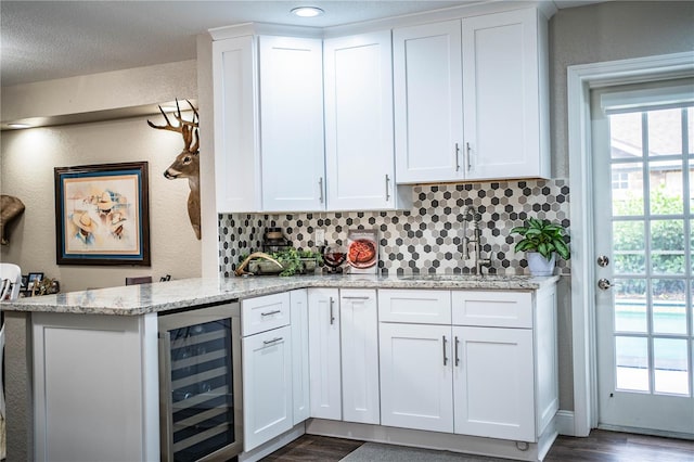 kitchen with tasteful backsplash, sink, white cabinetry, beverage cooler, and light stone counters