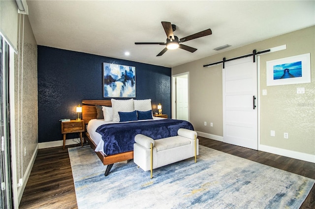 bedroom with ceiling fan, dark wood-type flooring, and a barn door