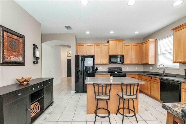 kitchen with a center island, black appliances, a kitchen bar, sink, and light tile patterned floors