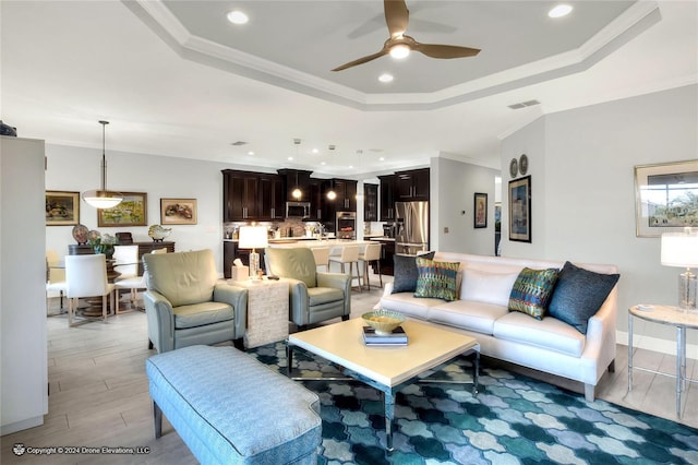 living room featuring ceiling fan, a tray ceiling, and crown molding