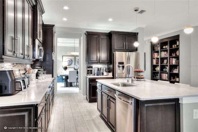 kitchen with a center island with sink, appliances with stainless steel finishes, tasteful backsplash, and hanging light fixtures