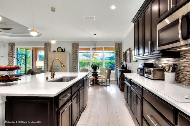 kitchen with stainless steel appliances, decorative backsplash, sink, hanging light fixtures, and a kitchen island with sink