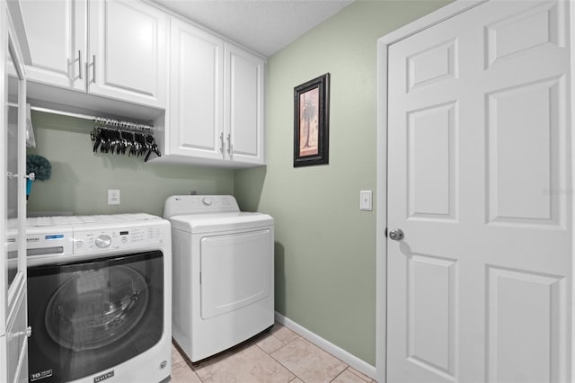 clothes washing area featuring light tile patterned floors, a textured ceiling, washing machine and clothes dryer, and cabinets