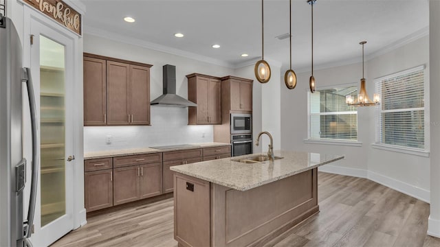 kitchen with an island with sink, sink, hanging light fixtures, stainless steel appliances, and wall chimney exhaust hood