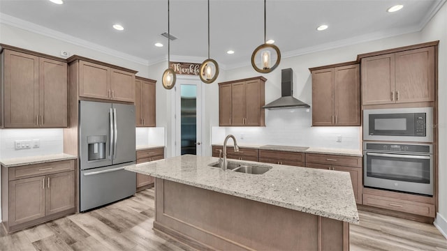 kitchen with wall chimney exhaust hood, sink, decorative light fixtures, appliances with stainless steel finishes, and a kitchen island with sink