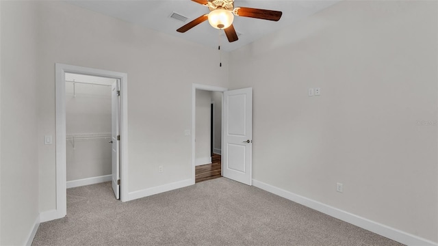 unfurnished bedroom featuring a walk in closet, light carpet, ceiling fan, and a closet