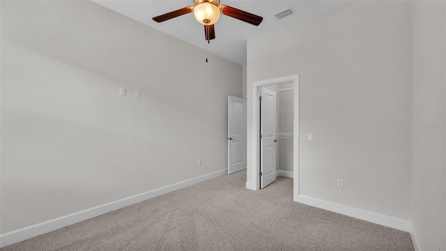 unfurnished bedroom with a walk in closet, light colored carpet, a closet, and ceiling fan