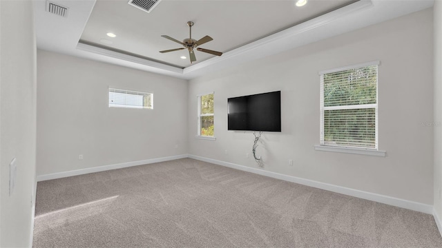 spare room featuring a tray ceiling, light colored carpet, and ceiling fan