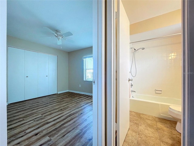 interior space with toilet, ceiling fan, and shower / washtub combination