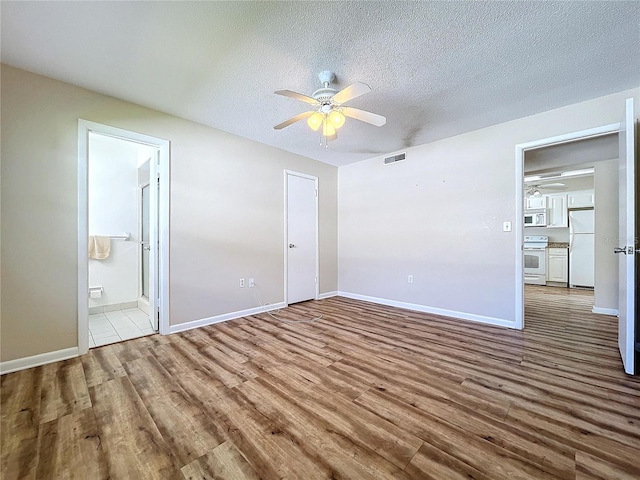 unfurnished bedroom featuring white fridge, hardwood / wood-style flooring, ceiling fan, ensuite bath, and a textured ceiling