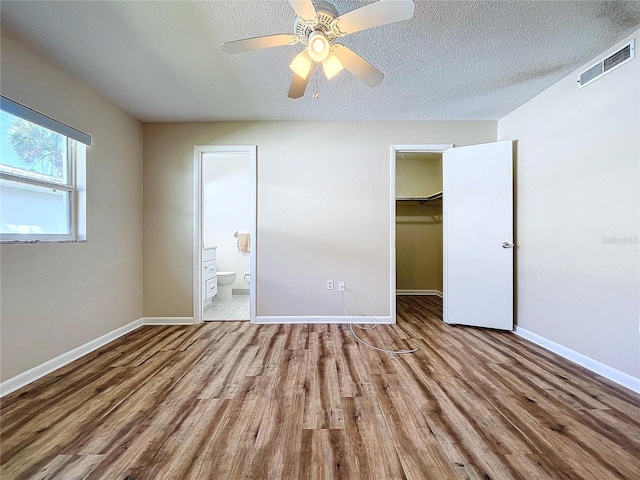 unfurnished bedroom with a spacious closet, connected bathroom, light hardwood / wood-style floors, a closet, and ceiling fan