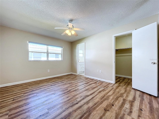 unfurnished bedroom featuring ceiling fan, wood-type flooring, a textured ceiling, a walk in closet, and a closet