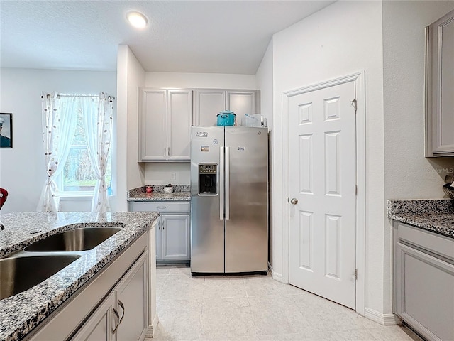 kitchen featuring sink, stainless steel fridge with ice dispenser, light stone counters, and gray cabinets