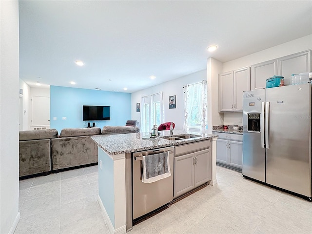 kitchen featuring sink, a kitchen island with sink, light stone countertops, appliances with stainless steel finishes, and gray cabinetry