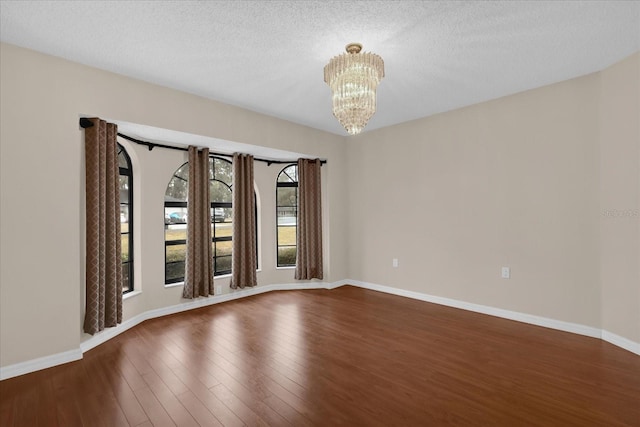 unfurnished room with dark wood-type flooring, an inviting chandelier, and a textured ceiling