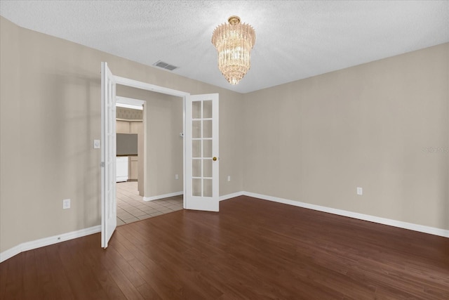 unfurnished room with french doors, an inviting chandelier, a textured ceiling, and wood-type flooring