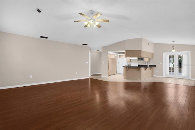 unfurnished living room with lofted ceiling, french doors, light wood-type flooring, and ceiling fan