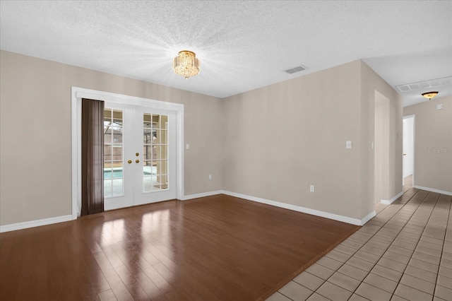 empty room featuring french doors, a notable chandelier, a textured ceiling, and hardwood / wood-style flooring