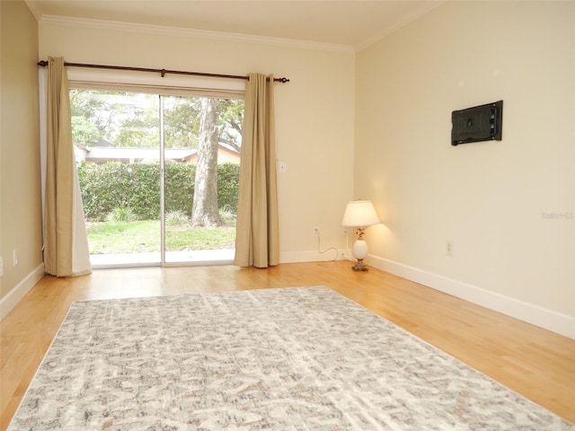 spare room with ornamental molding, baseboards, and light wood finished floors