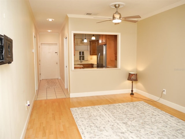 hallway with light wood-type flooring, baseboards, visible vents, and ornamental molding