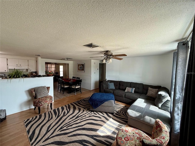 living room with light wood-type flooring, ceiling fan, and a textured ceiling