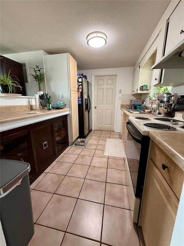 kitchen with electric range, sink, light tile patterned floors, white cabinets, and stainless steel fridge