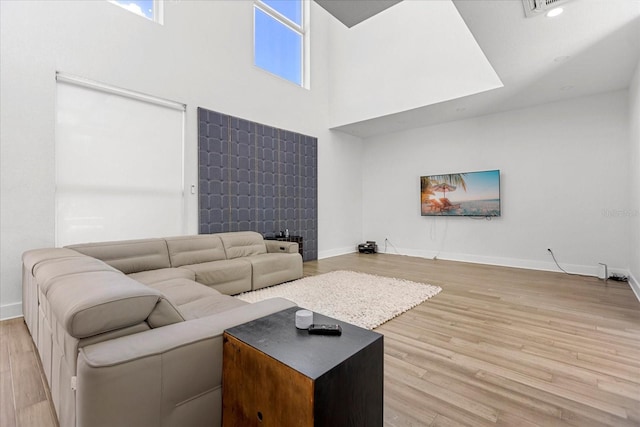 living room with a wealth of natural light, light hardwood / wood-style flooring, and a towering ceiling