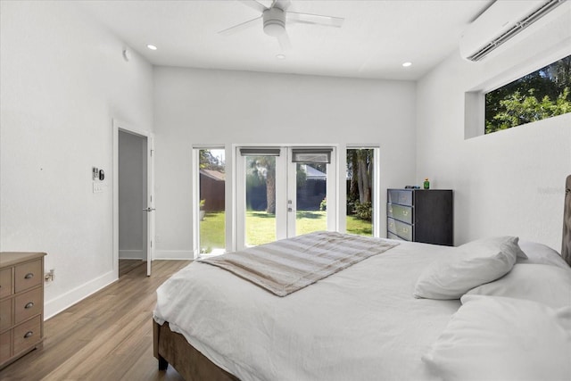 bedroom featuring ceiling fan, a wall mounted AC, light hardwood / wood-style floors, access to outside, and french doors