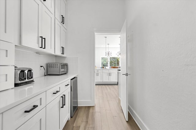 bar with tasteful backsplash, white cabinets, light wood-type flooring, and beverage cooler