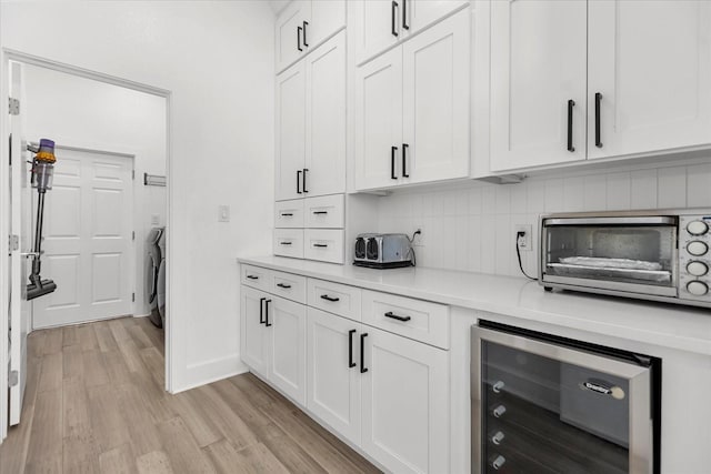 kitchen with wine cooler, backsplash, washer / clothes dryer, white cabinetry, and light hardwood / wood-style flooring