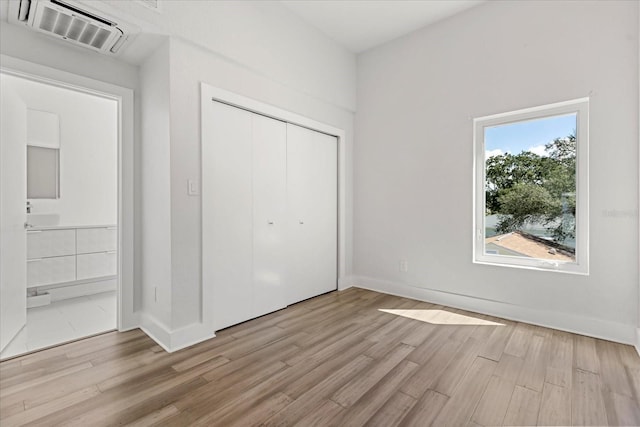 unfurnished bedroom with a closet, light hardwood / wood-style floors, and ensuite bath